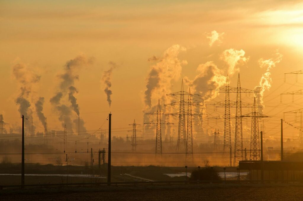 Silhouette of power lines and industrial smoke at sunset, highlighting pollution and energy themes.